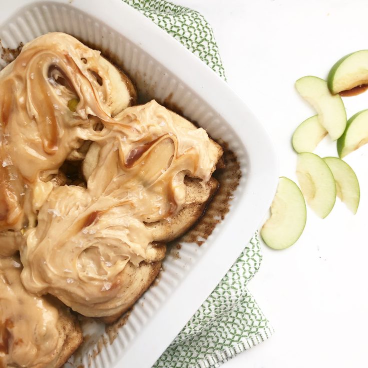 cinnamon rolls in a white baking dish with caramel frosting on a white background.