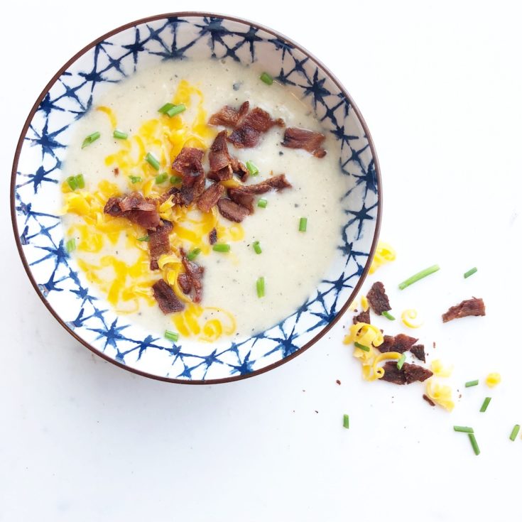 loaded potato soup in blue bowl topped with cheddar cheese, bacon and chives