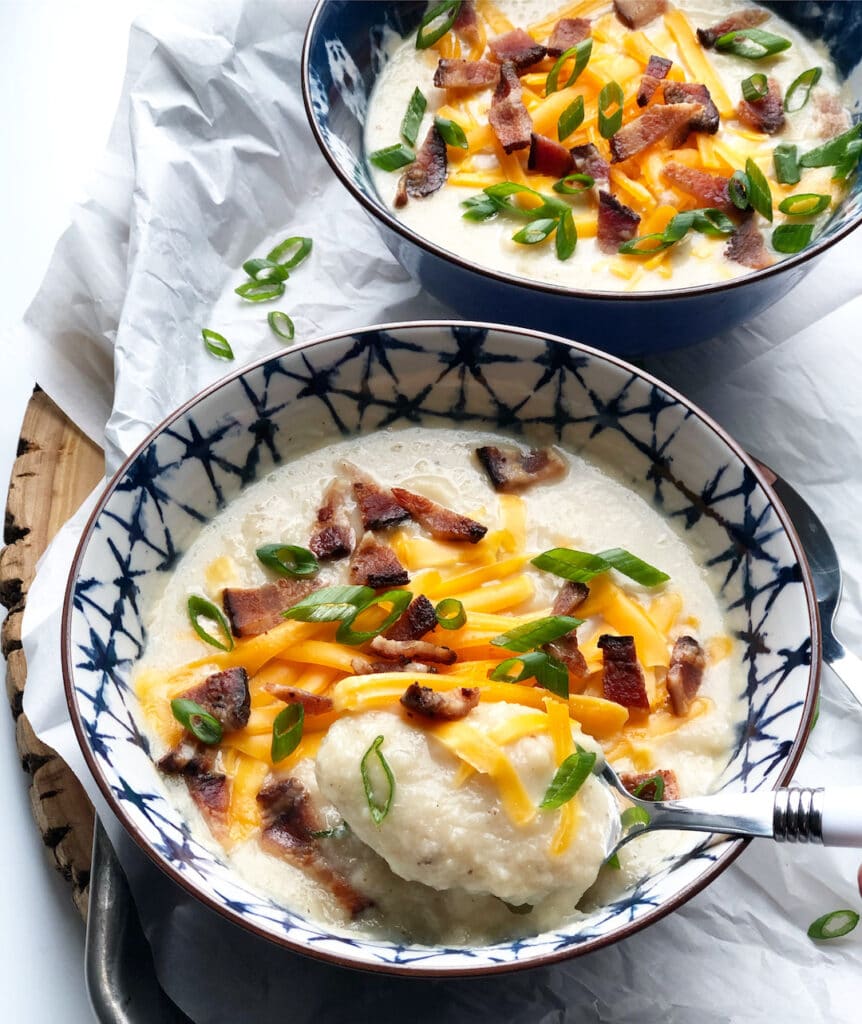 potato soup in blue bowls with cheddar cheese, chives and bacon
